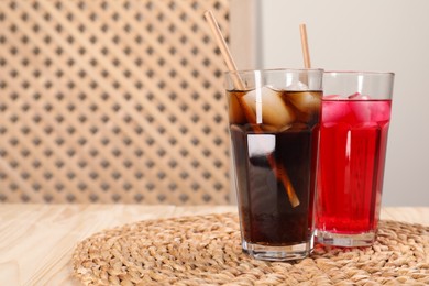 Glasses of different refreshing soda water with ice cubes and straws on wooden table, space for text