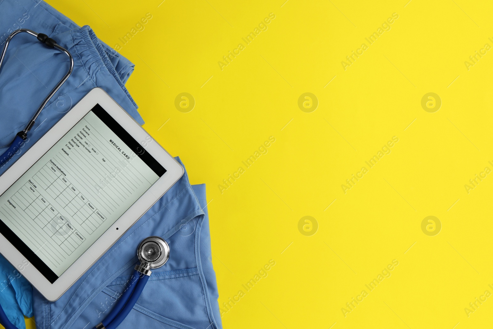 Photo of Medical uniform, tablet and stethoscope on yellow background, flat lay. Space for text
