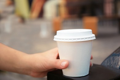 Woman with cardboard cup of coffee outdoors, closeup