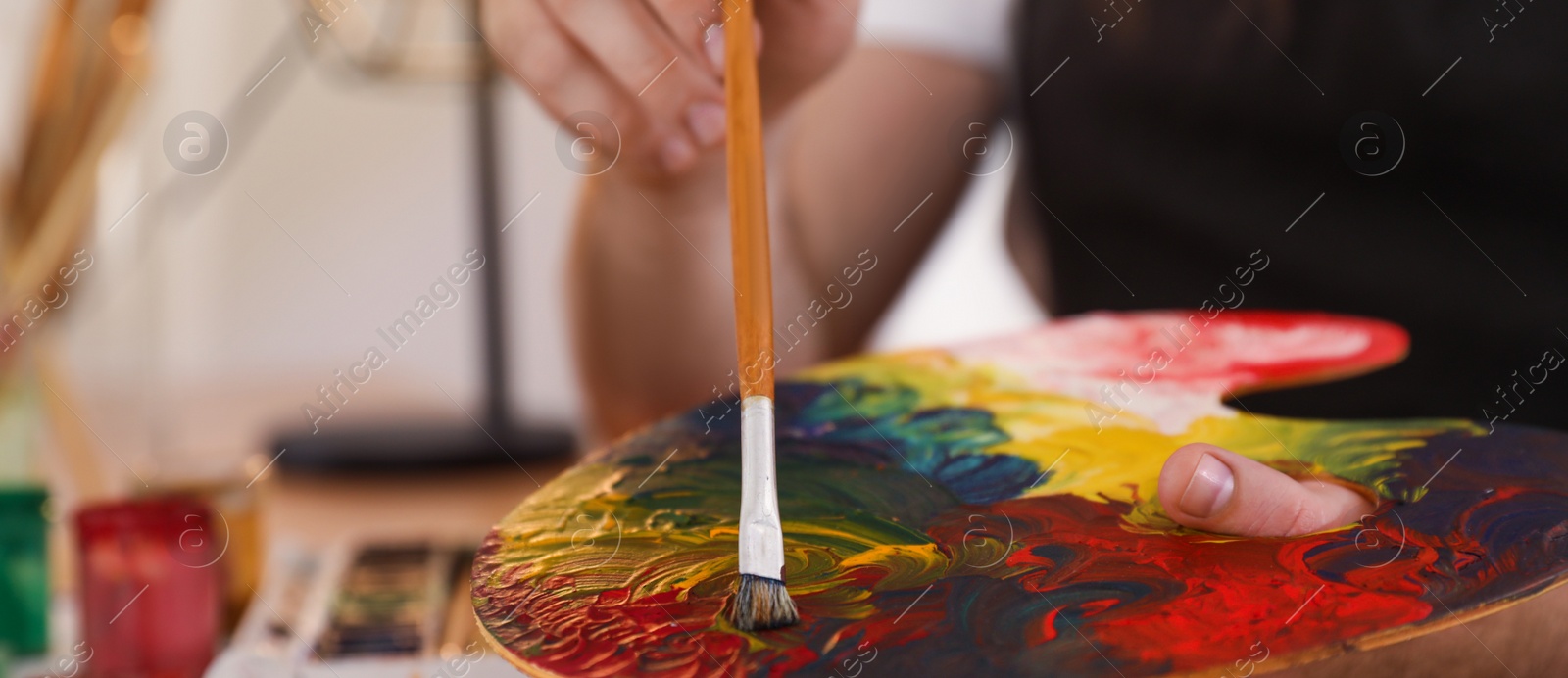 Image of Young man with painting tools at table in artist studio, closeup. Banner design