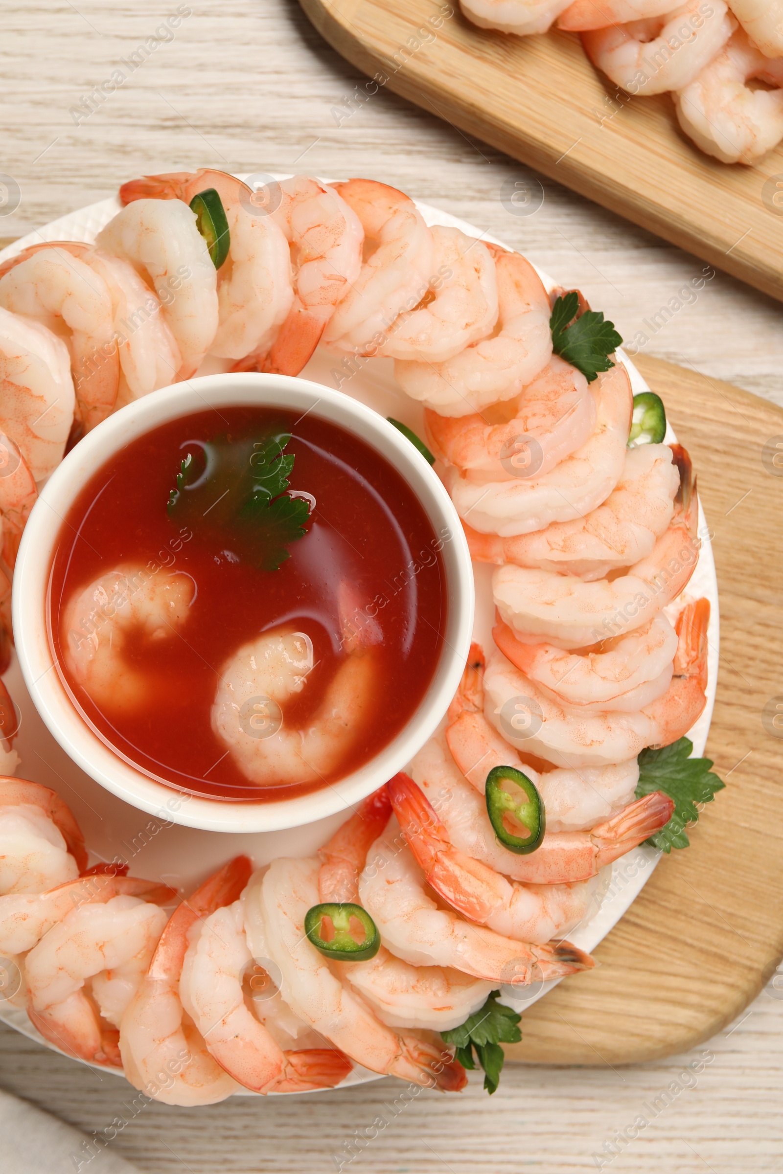 Photo of Tasty boiled shrimps with cocktail sauce, chili and parsley on light wooden table, flat lay