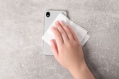 Photo of Woman wiping smartphone with paper towel at gray table, top view