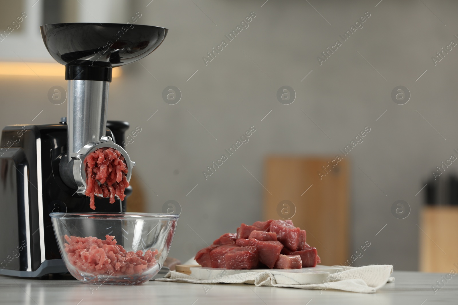 Photo of Electric meat grinder with beef mince on white table in kitchen, space for text