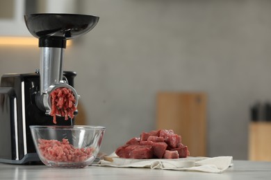 Electric meat grinder with beef mince on white table in kitchen, space for text