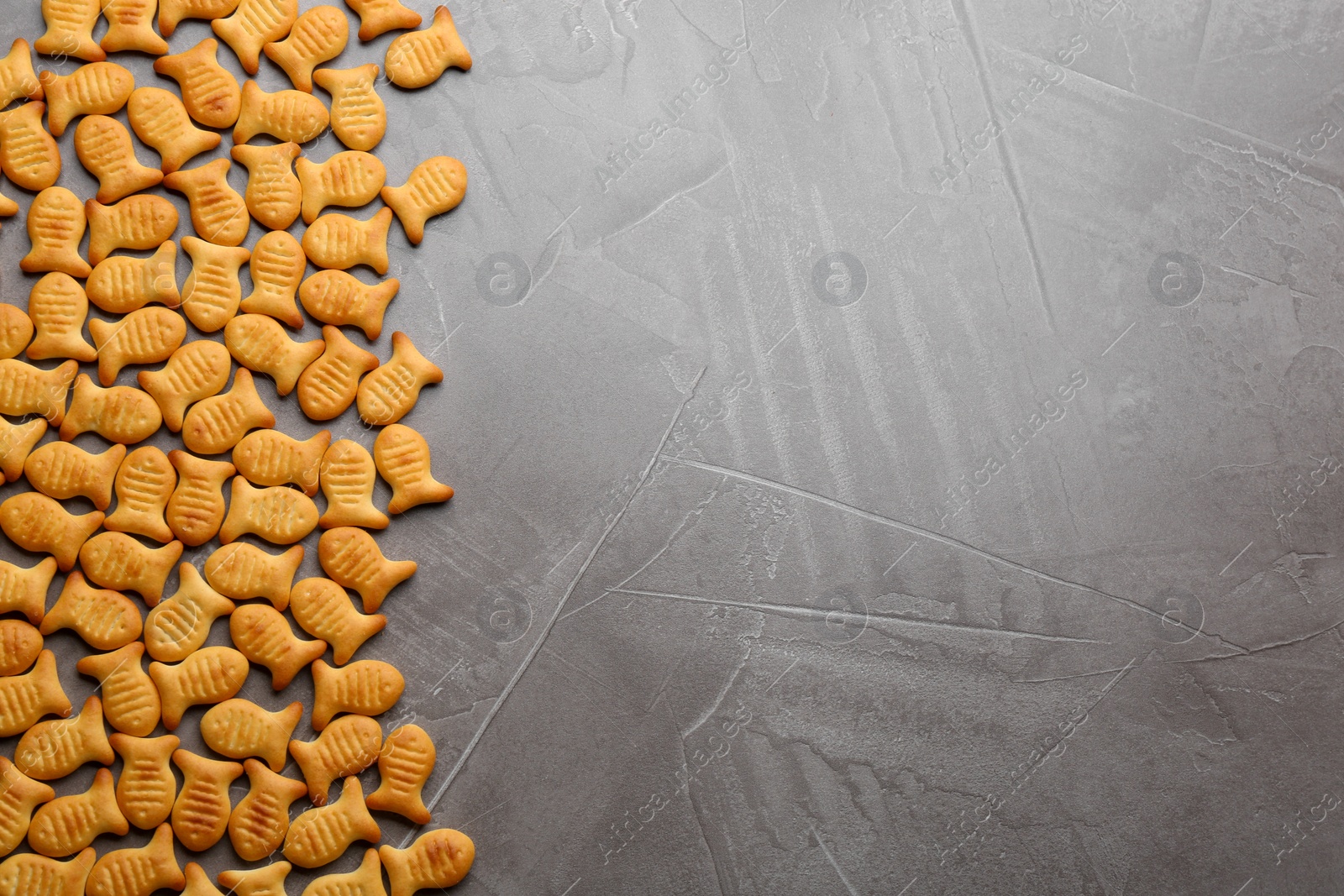 Photo of Delicious goldfish crackers on grey table, flat lay. Space for text