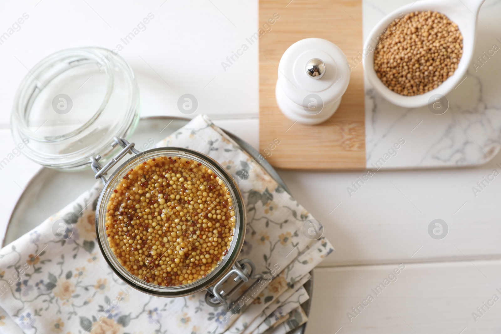 Photo of Jar and spoon of whole grain mustard on white wooden table, flat lay. Space for text