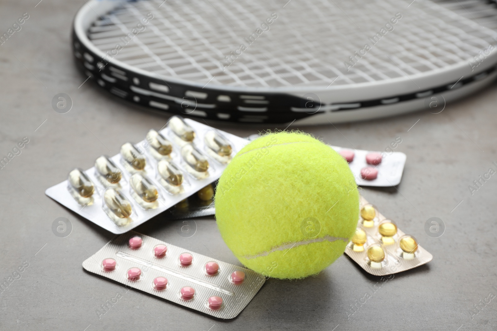 Photo of Tennis ball, racket and different pills on light grey table, closeup. Doping concept