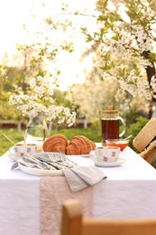 Photo of Stylish table setting with tea and croissants in spring garden