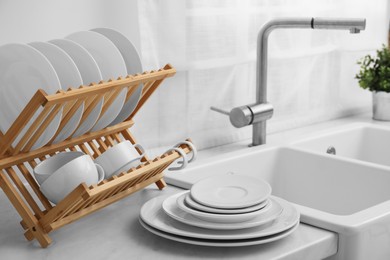 Drying rack with clean dishes on light marble countertop near sink in kitchen