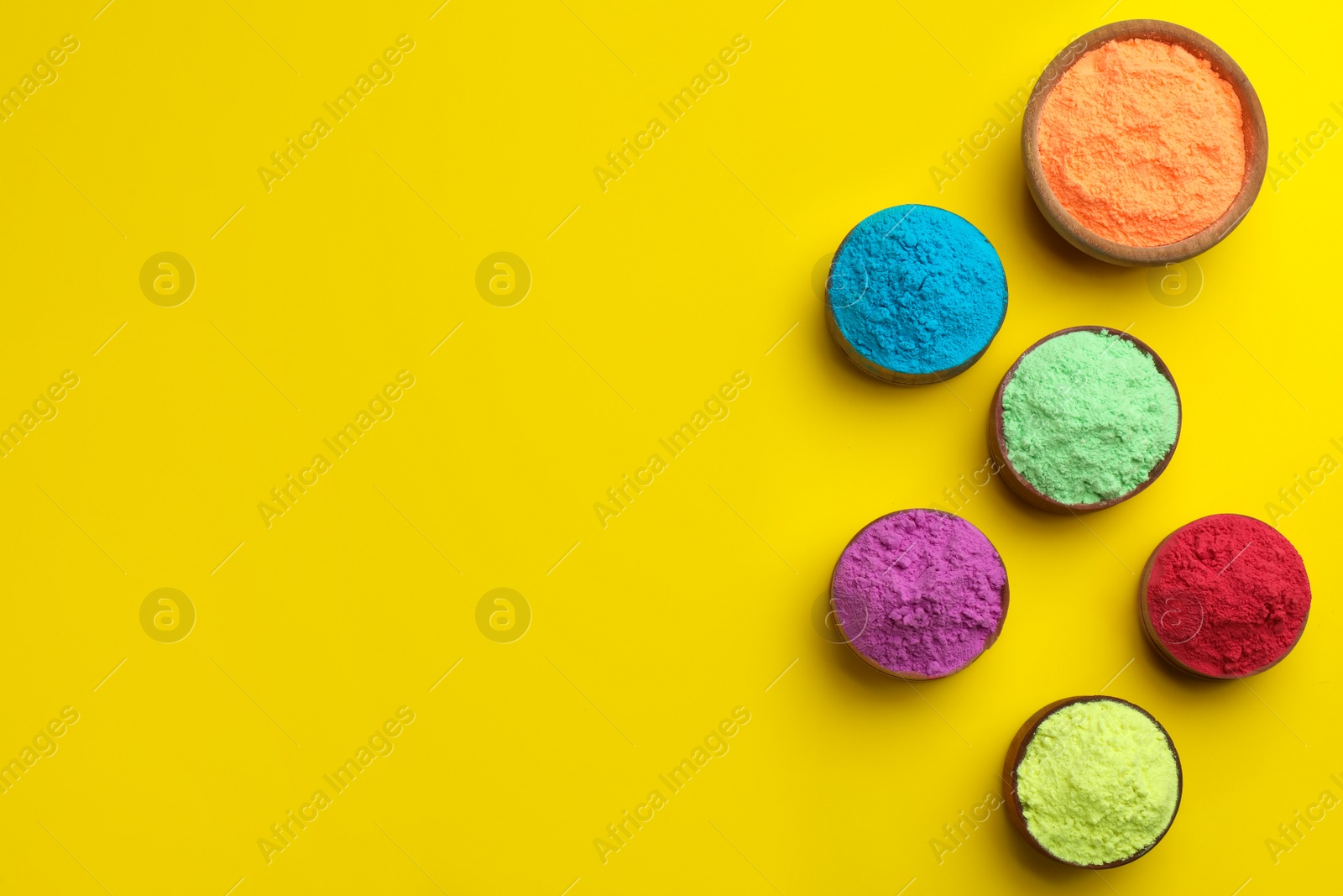 Photo of Colorful powders in bowls on yellow background, flat lay with space for text. Holi festival celebration