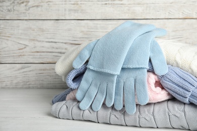 Photo of Stacked sweaters and gloves on wooden table, closeup. Autumn clothes