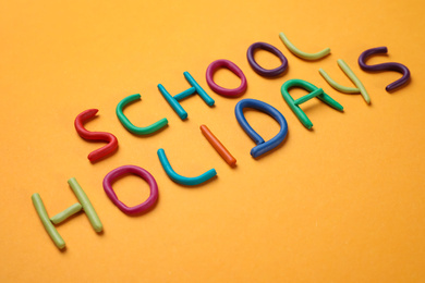 Photo of Phrase School Holidays made of modeling clay on orange background