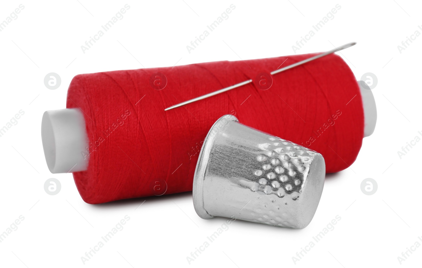 Photo of Thimble and spool of red sewing thread with needle isolated on white