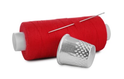 Photo of Thimble and spool of red sewing thread with needle isolated on white