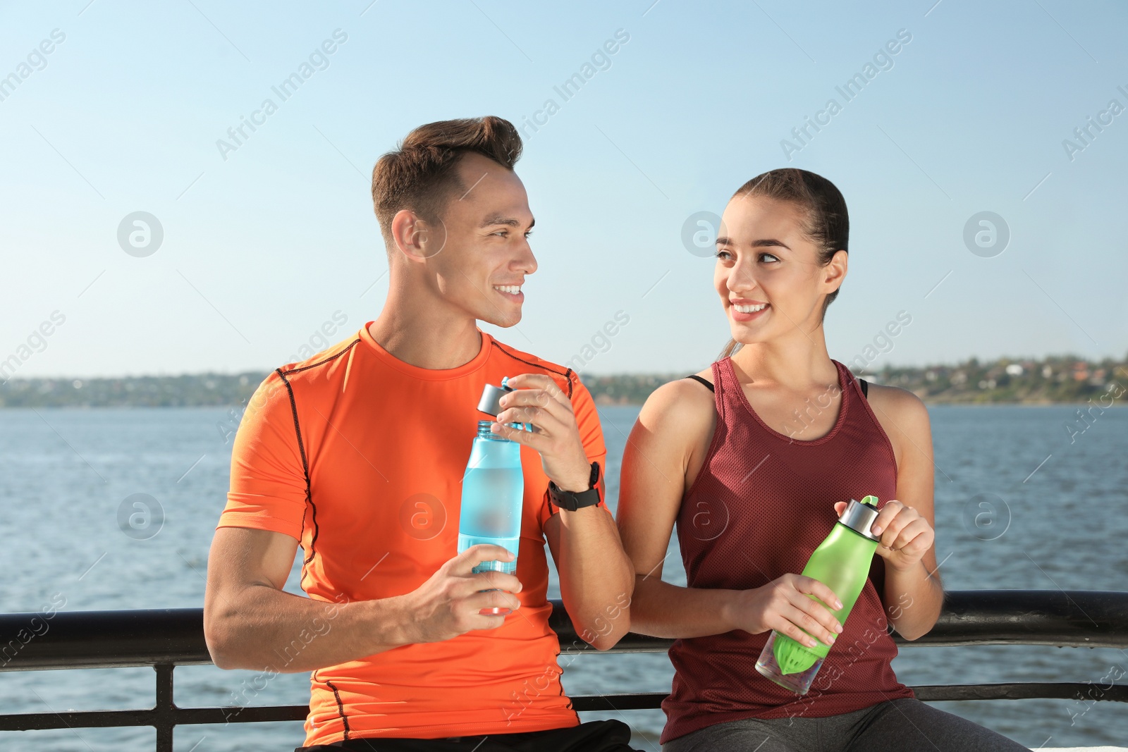 Photo of Young sporty couple with bottles of water outdoors on sunny day