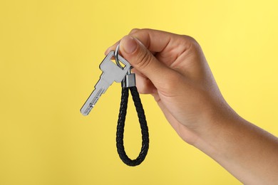 Photo of Woman holding key with black leather keychain on yellow background, closeup