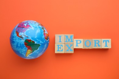 Globe, words Import and Export made of wooden cubes on orange background, flat lay