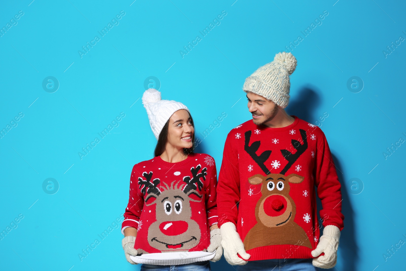 Photo of Young couple in Christmas sweaters and knitted hats on color background