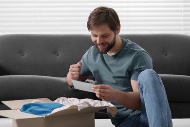 Photo of Happy man with greeting card near parcel at home. Internet shopping