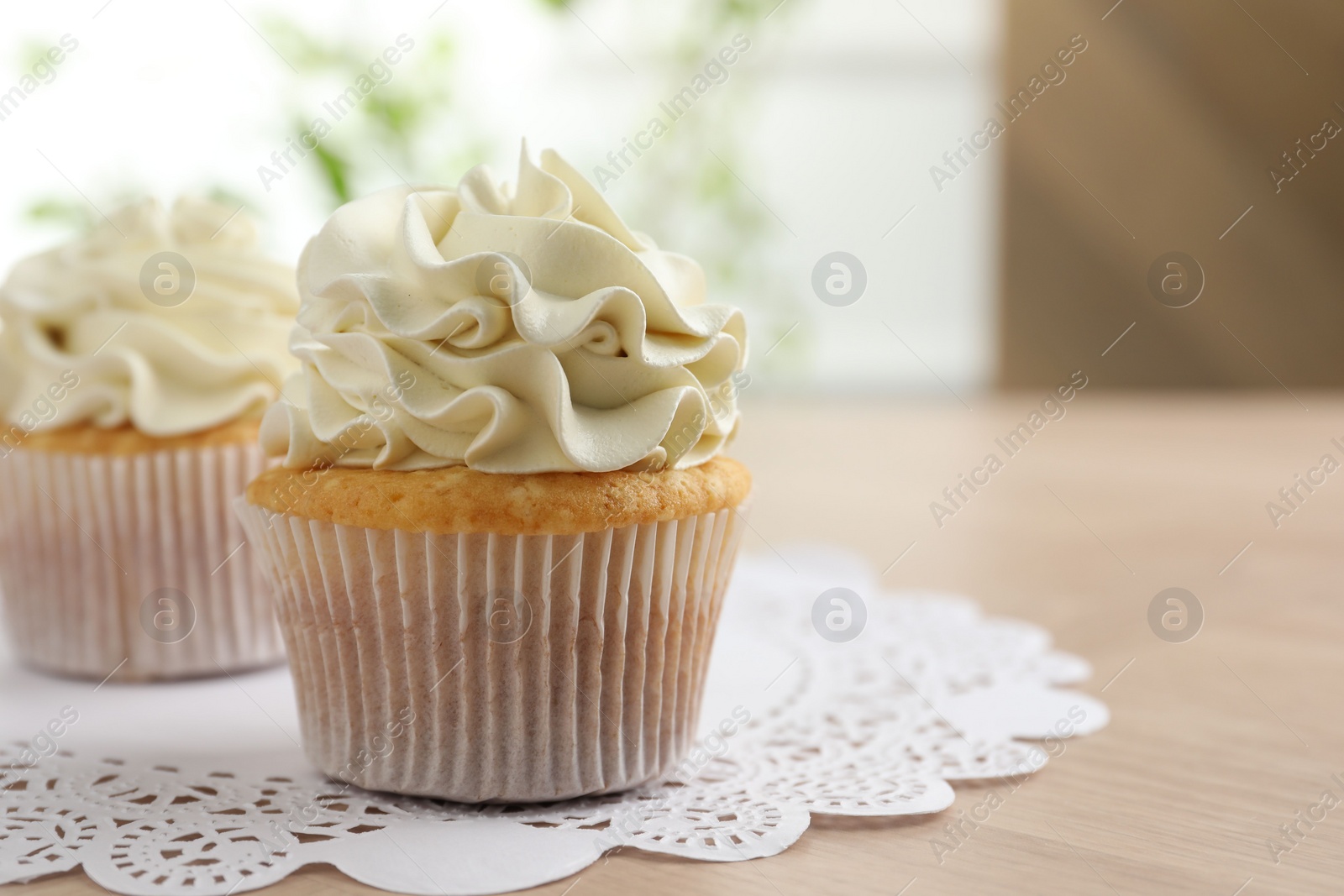 Photo of Tasty cupcakes with vanilla cream on light wooden table, closeup