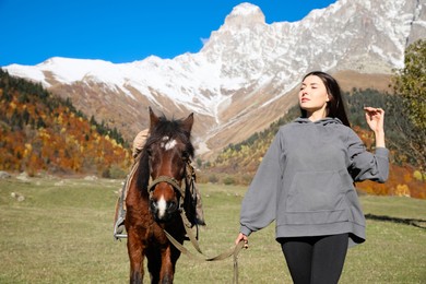 Photo of Young woman walking with horse in mountains on sunny day. Beautiful pet