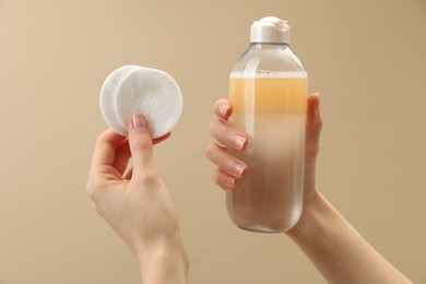 Woman holding makeup remover and cotton pads on beige background, closeup