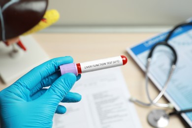Photo of Laboratory worker holding tube with blood sample and label Liver Function Test over table, closeup