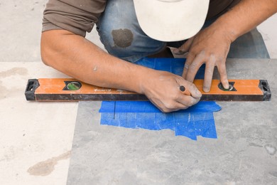 Photo of Worker making holes for bathroom water pipes in tile indoors, closeup