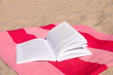 Photo of Open book and striped towel on sandy beach