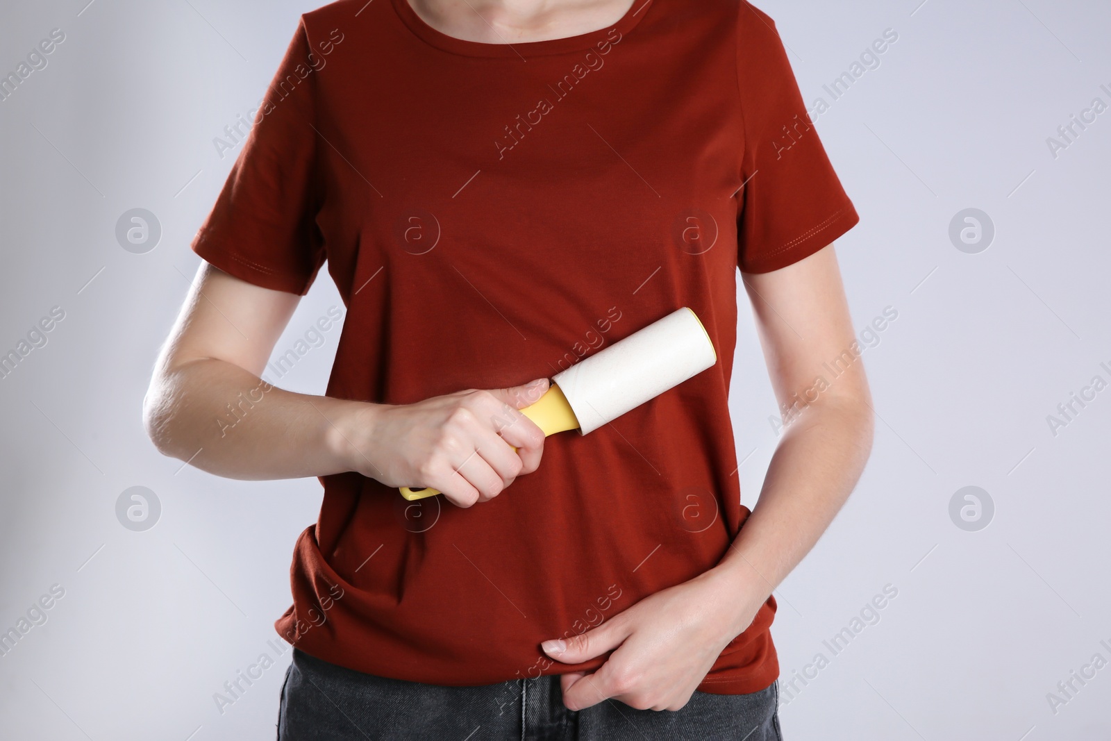 Photo of Woman cleaning red t-shirt with lint roller on grey background, closeup