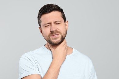 Photo of Man suffering from sore throat on light gray background