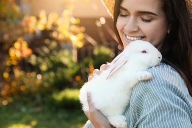 Photo of Happy woman with cute rabbit outdoors on sunny day, closeup. Space for text