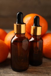 Bottles of tangerine essential oil and fresh fruits on wooden table, closeup