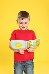 Photo of Cute little boy reading book on color background