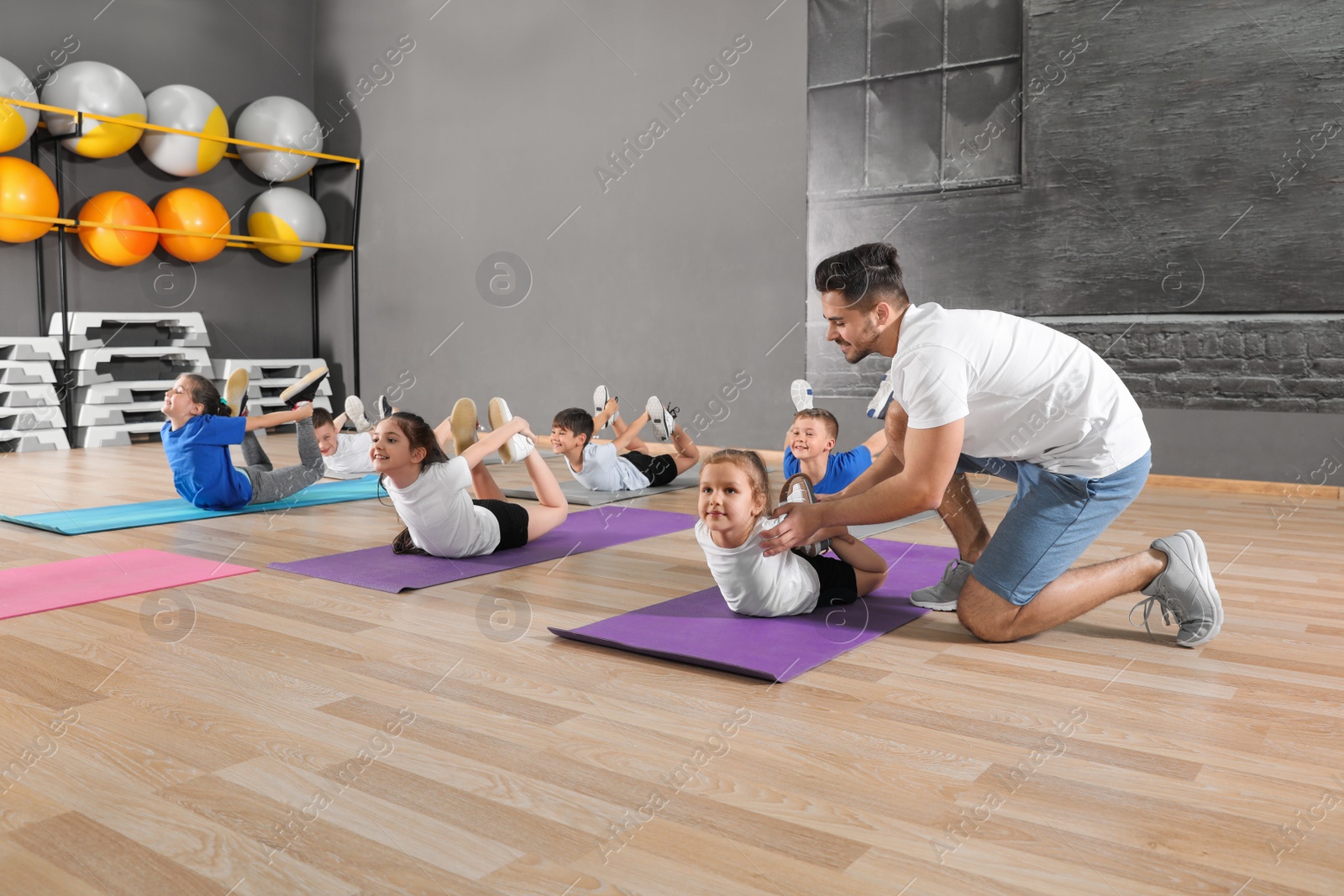 Photo of Trainer helping children to do physical exercise in school gym. Healthy lifestyle