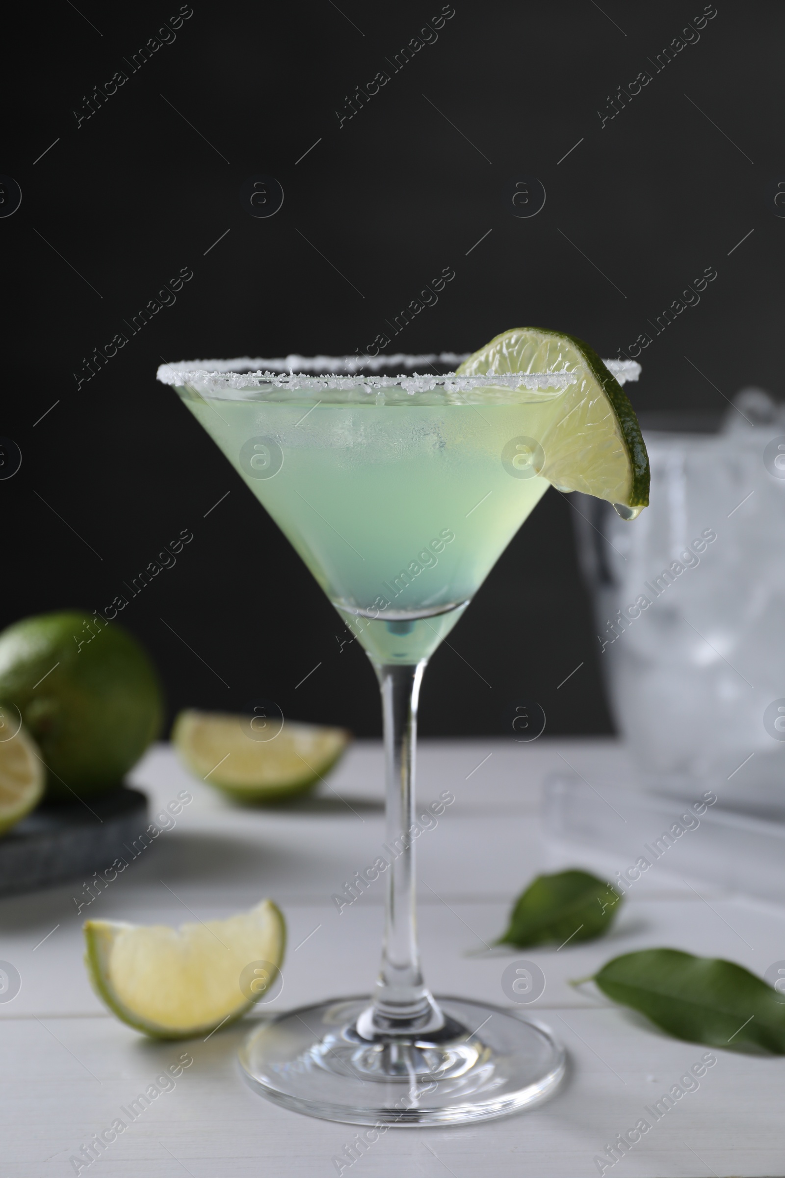 Photo of Delicious Margarita cocktail in glass and limes on white wooden table