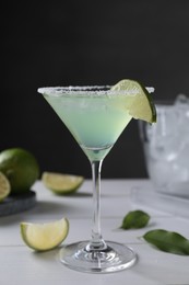 Photo of Delicious Margarita cocktail in glass and limes on white wooden table