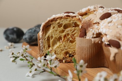 Photo of Pieces of delicious Italian Easter dove cake (traditional Colomba di Pasqua), branch with flowers and painted eggs on light grey table, closeup