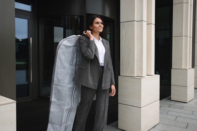 Photo of Attractive happy businesswoman holding garment cover with clothes outdoors. Dry cleaning service