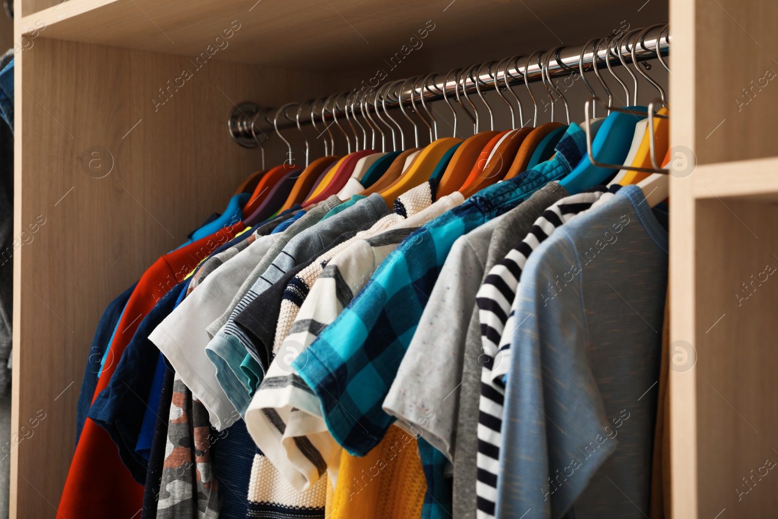 Photo of Hangers with teenage clothes on rack in wardrobe, closeup