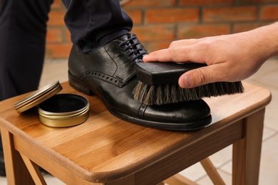 Photo of Man shining client's shoe on wooden stool indoors, closeup