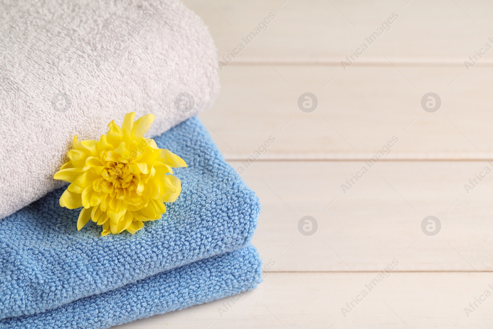 Photo of Closeup view of soft folded towels and chrysanthemum on white wooden table, space for text