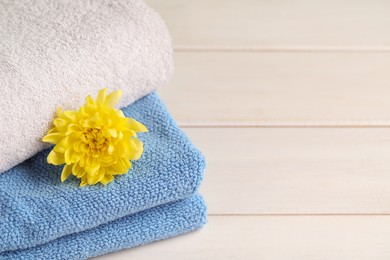 Closeup view of soft folded towels and chrysanthemum on white wooden table, space for text