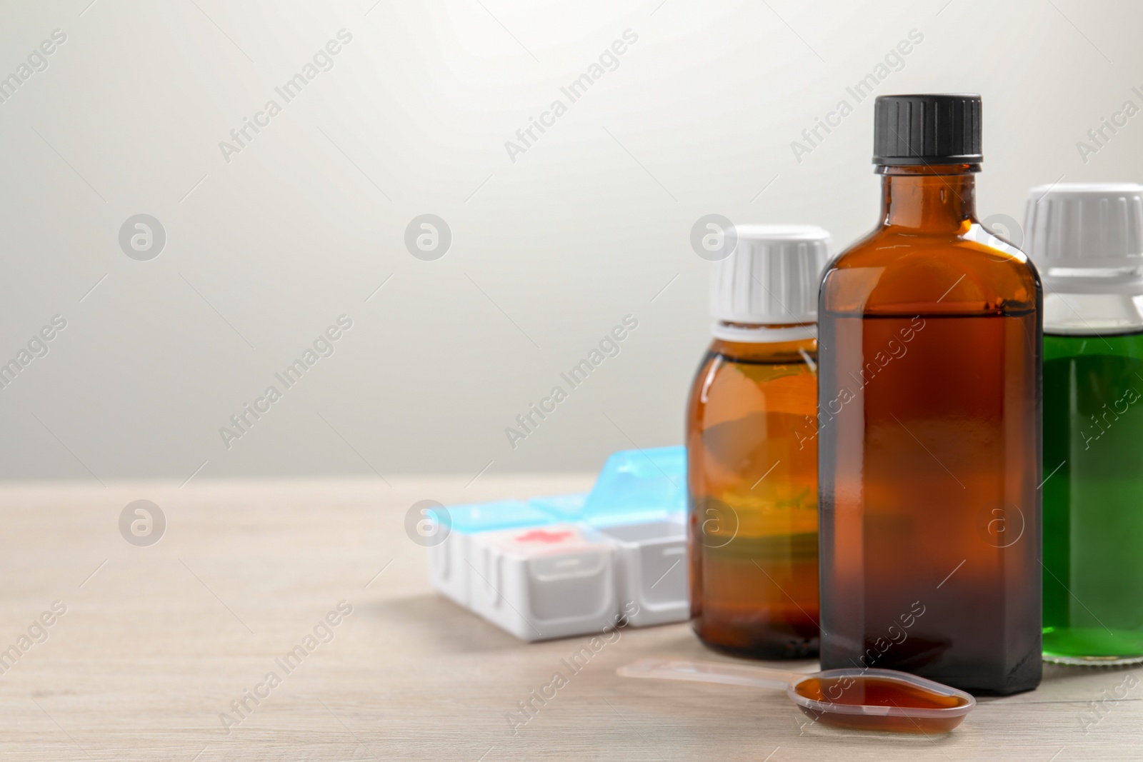 Photo of Bottles of syrup, dosing spoon and weekly pill organizer on table against white background, space for text. Cold medicine