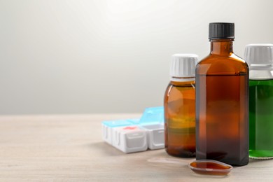 Photo of Bottles of syrup, dosing spoon and weekly pill organizer on table against white background, space for text. Cold medicine