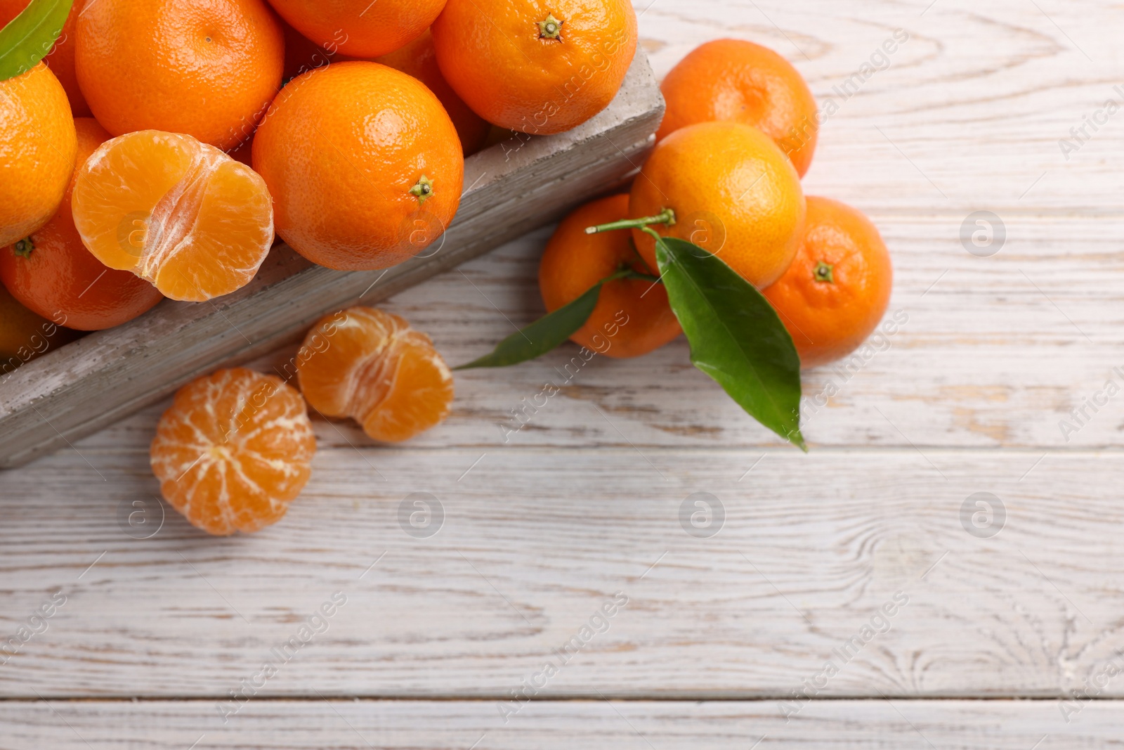 Photo of Delicious tangerines with leaves on light wooden table, top view. Space for text