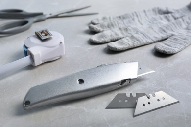 Photo of Utility knife, blades and measuring tape on light grey table, closeup