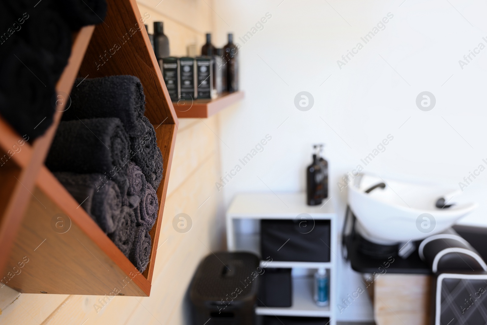 Photo of Shelves with rolled towels and professional hair cosmetics on wall in barbershop, closeup