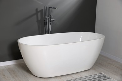 Photo of Stylish ceramic tub near grey wall in bathroom