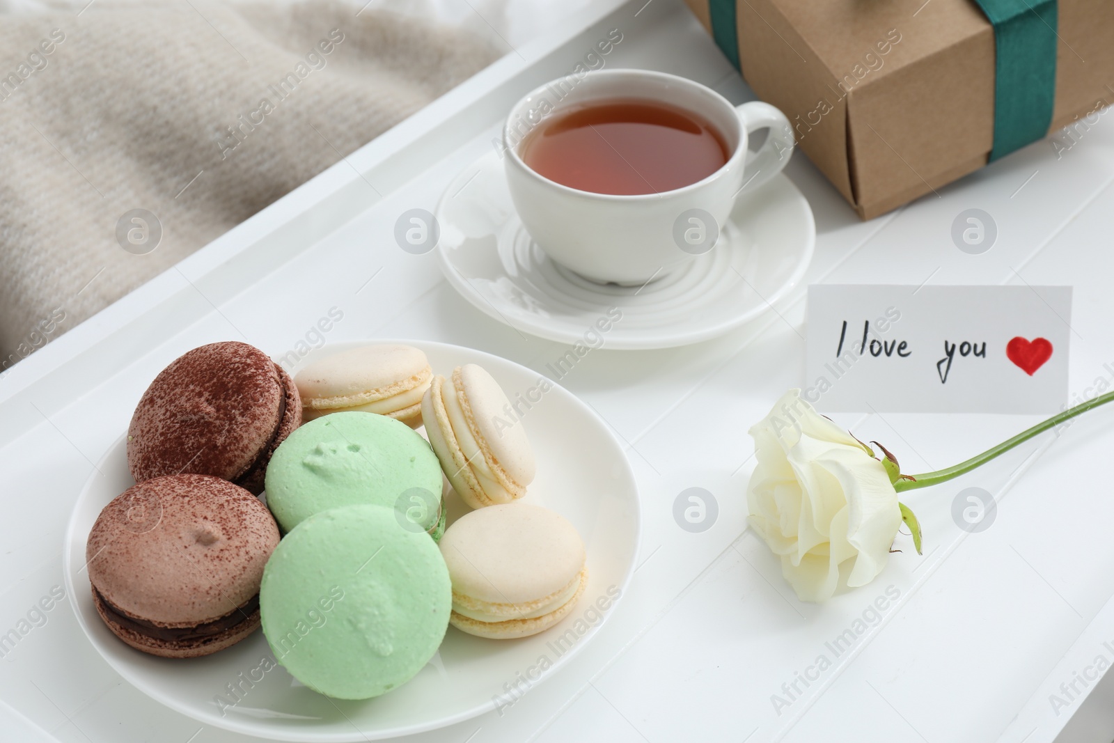 Photo of Tasty breakfast served in bed. Delicious macarons, tea, gift box, rose and I Love You card on tray